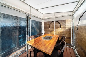 A covered outdoor dining area with a wooden table and chairs, a metal sink, and a view through a glass wall. - Gyeongju Sanmaru Pension (Gyeongju)