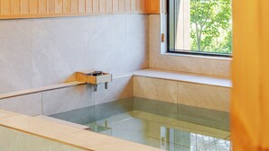 A modern bathroom with a glass-enclosed bathtub, wooden cabinetry, and a window providing a view of greenery. - Gyeongju Sanmaru Pension (Gyeongju)