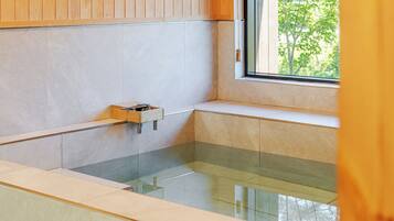 Un baño moderno con bañera acristalada, muebles de madera y una ventana con vistas a la vegetación.