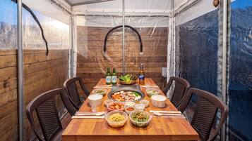 Un tavolo da pranzo imbandito per quattro, con diversi piatti, bottiglie e una griglia all'interno di una struttura a tenda.