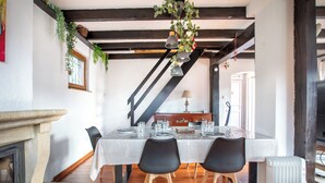 Un coin repas avec une table dressée pour quatre personnes, des chaises en bois, une nappe blanche et une plante suspendue.