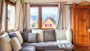 Un salon chaleureux avec un canapé gris, un meuble en bois et une vue sur une maison par la fenêtre.