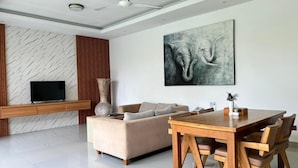 Una sala de estar moderna con un sofá, una mesa de comedor de madera y un televisor de pantalla plana montado en una pared con diseño de mármol.