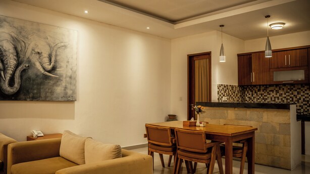 Un comedor con una mesa y sillas de madera, un cuadro en la pared, y una cocina con armarios de madera y un salpicadero de azulejos.