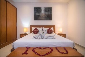 A hotel room with a neatly made bed, two bedside lamps, a painting on the wall, and a heart-shaped arrangement of rose petals on the table. - Kubu Manggala 1-Bedroom Private Pool Villa Include Breakfast (Kerobokan Kelod, Badung)