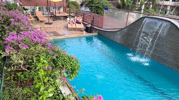 A swimming pool with a waterfall feature, surrounded by lush greenery and a lounge area with sun loungers. - Beach Corridor Residence (Negombo)