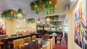 A restaurant with multiple dining tables, chairs, hanging plants, and artwork on the walls. - Beach Corridor Residence (Negombo)