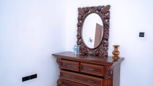 Une commode en bois sur laquelle sont posés un miroir, un vase et une bouteille.