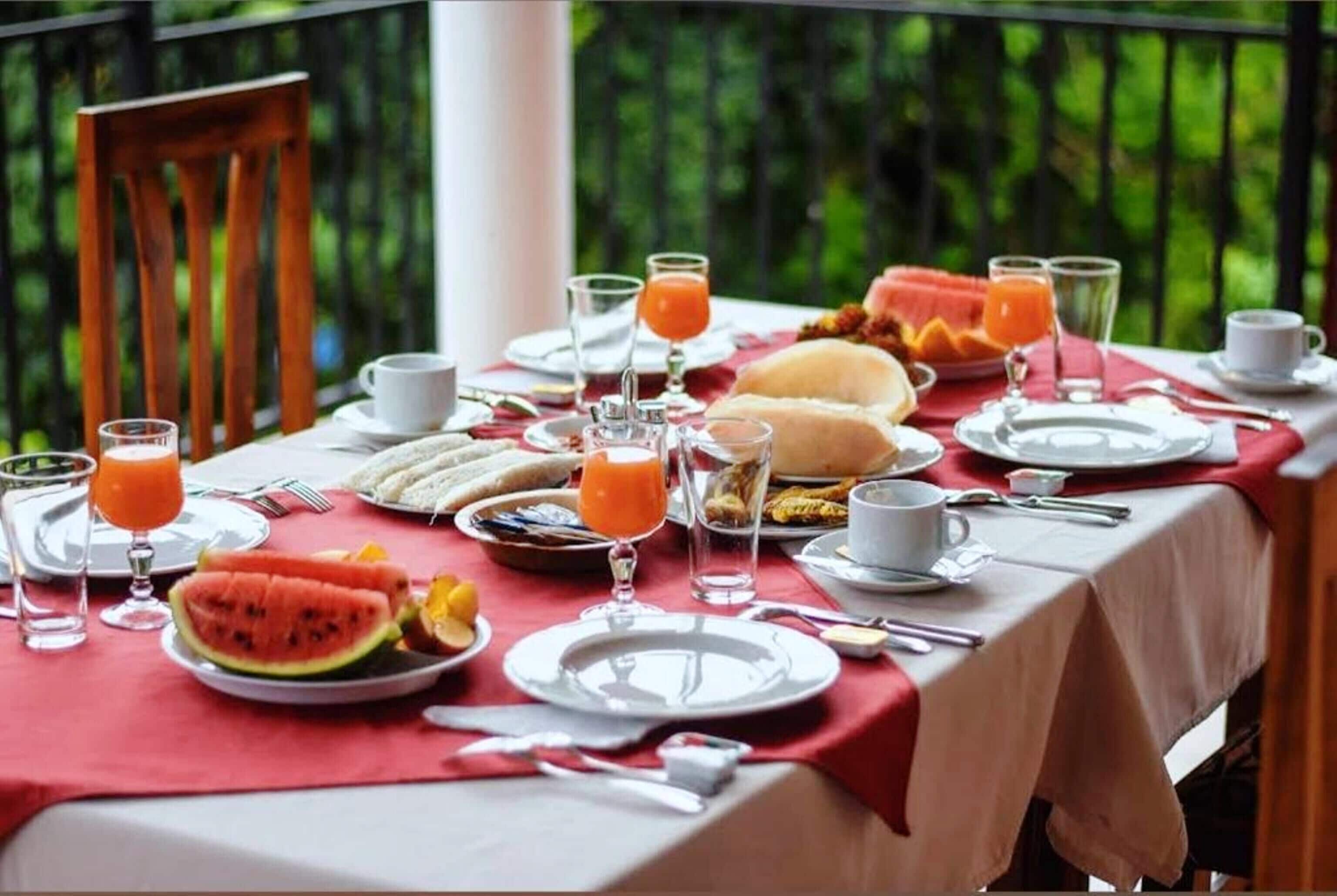A breakfast table set outdoors with plates, glasses, and a watermelon slice.