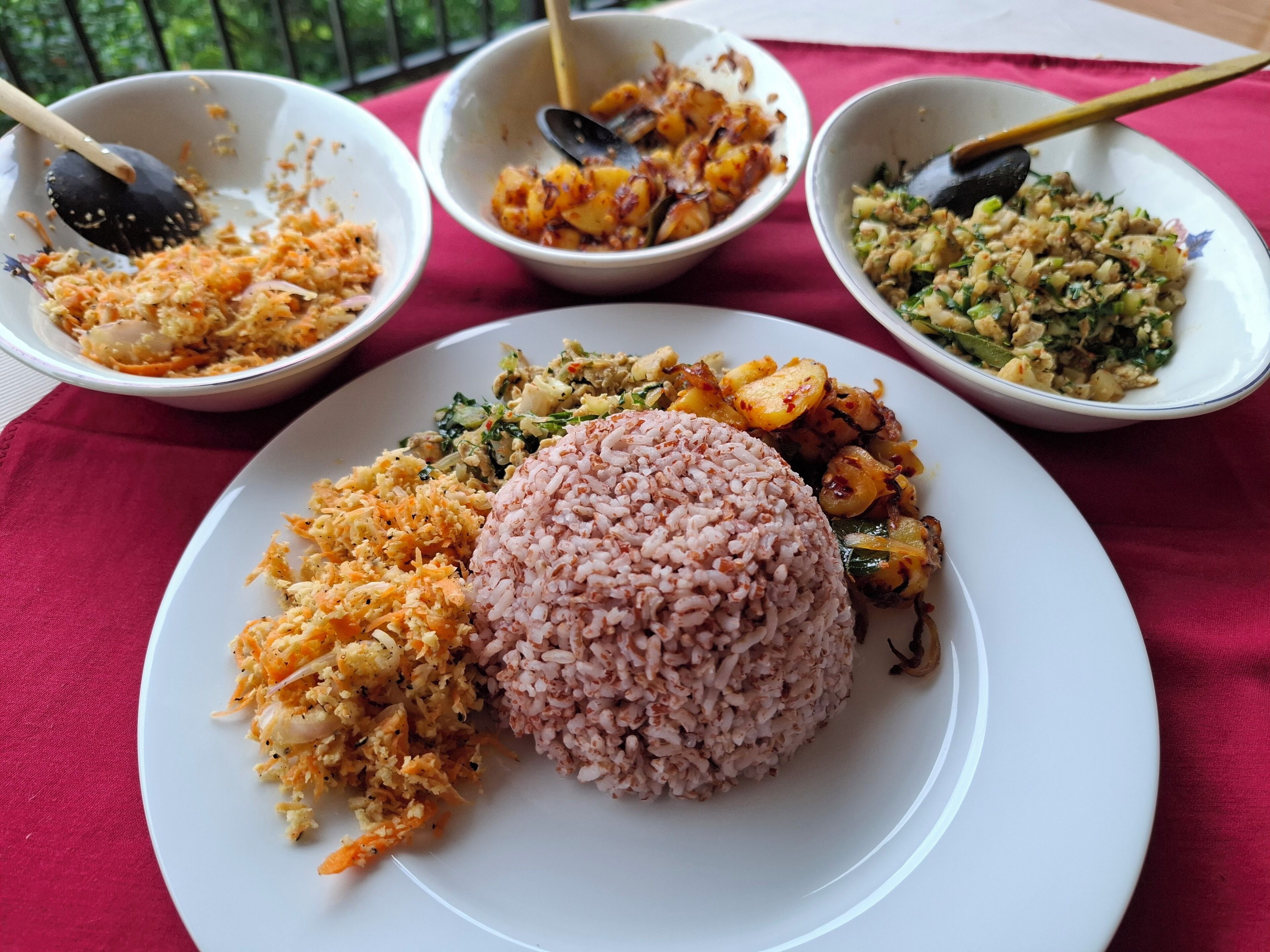 A plate with a mound of pink rice, a side of shredded carrots, and two bowls of mixed vegetables.