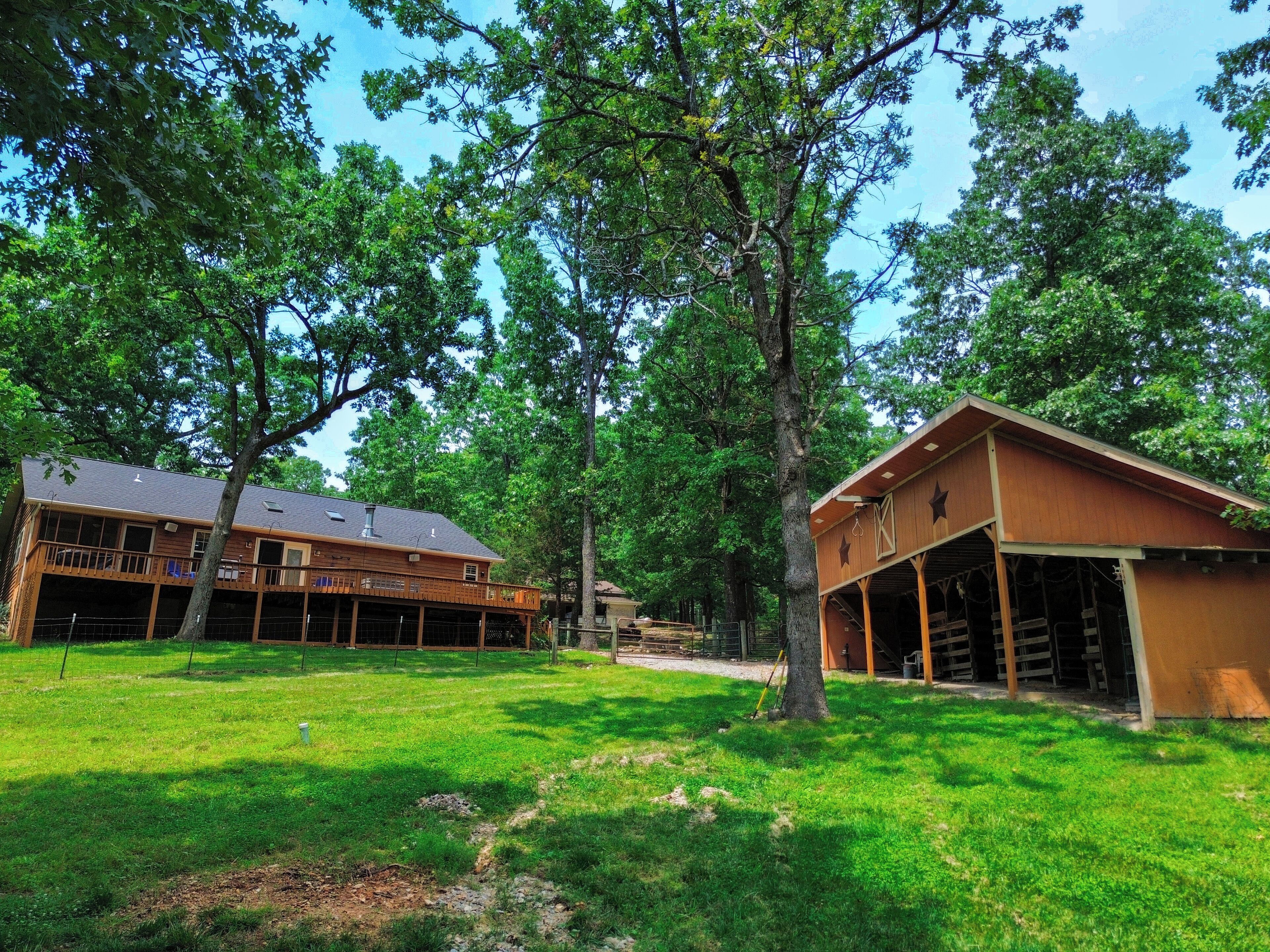 A two-story wooden cabin with a balcony, surrounded by lush green trees and a well-maintained lawn.