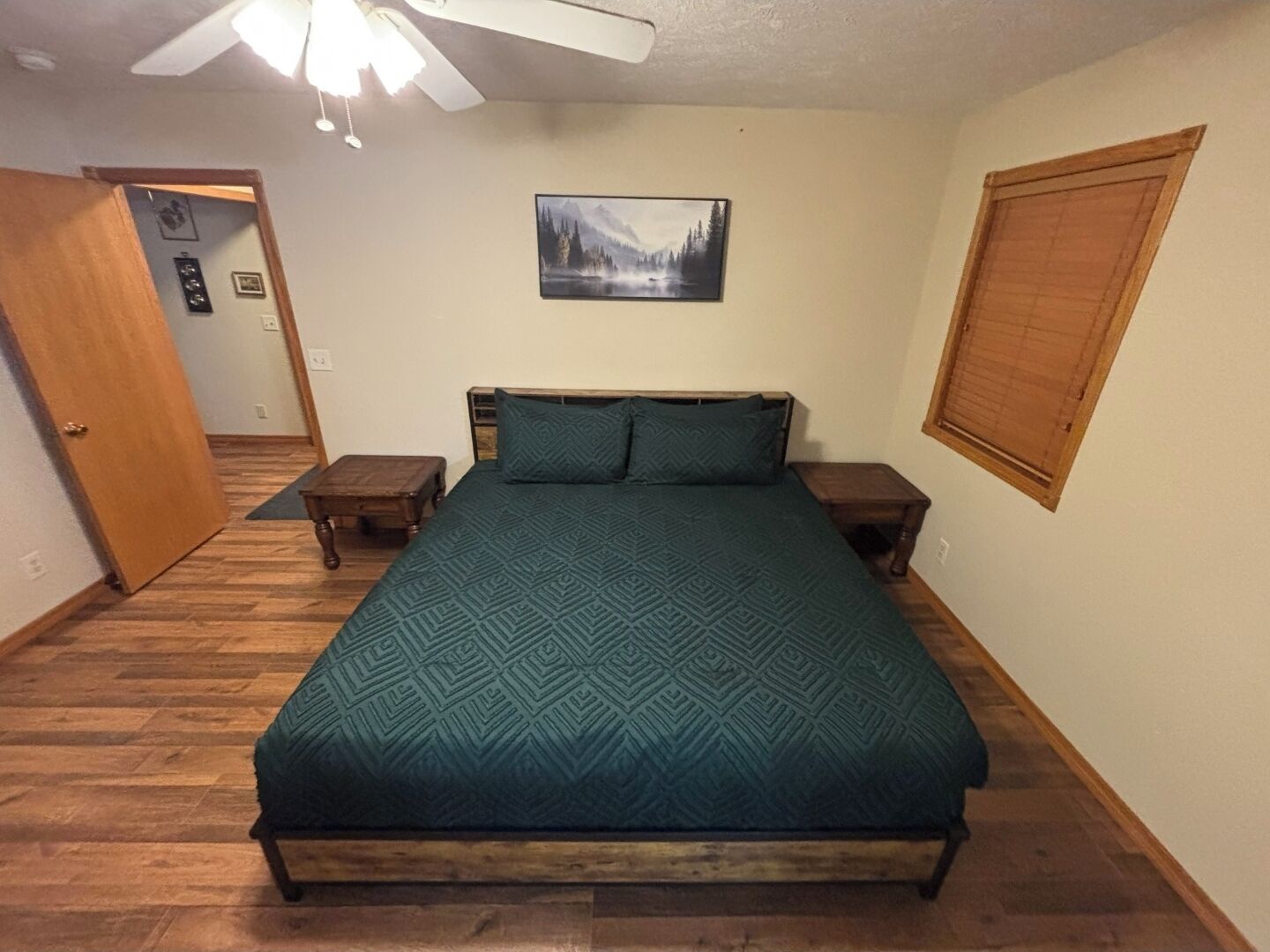 A bedroom with a bed, wooden headboard, two nightstands, a wall-mounted picture, and a door.