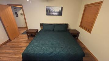 A bedroom with a bed, wooden headboard, two nightstands, a wall-mounted picture, and a door.