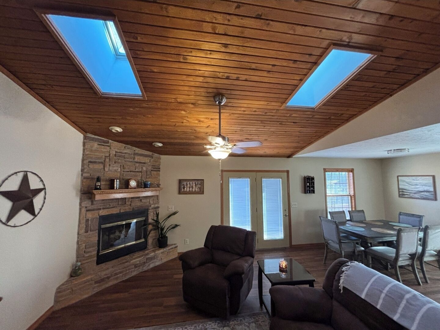 A living room with a stone fireplace, wooden ceiling, and skylights.