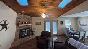 A living room with a stone fireplace, wooden ceiling, and skylights. - Rustic Retreat near Norfork Lake (Clarkridge)