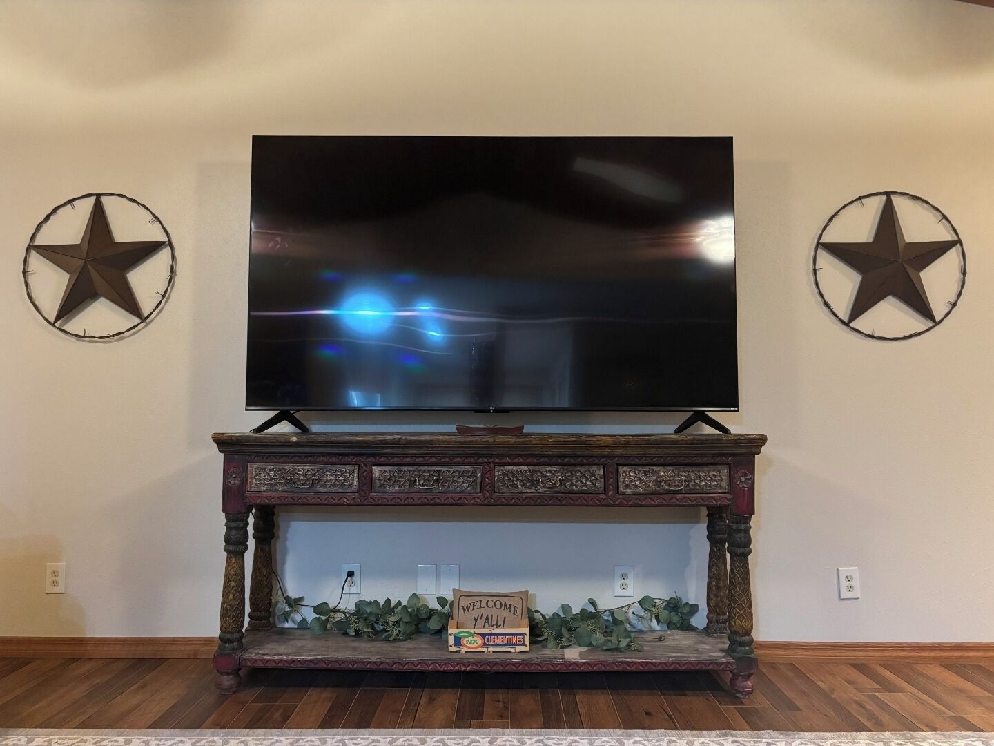 A flat-screen TV mounted on a wooden console table with decorative elements and a welcome sign.