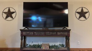 A flat-screen TV mounted on a wooden console table with decorative elements and a welcome sign. - Rustic Retreat near Norfork Lake (Clarkridge)