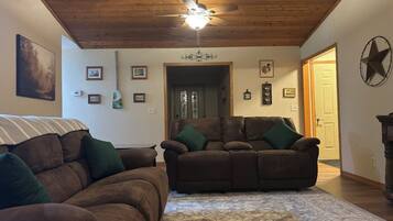 A living room with two brown leather sofas, a patterned rug, wooden ceiling, and a door leading to another room.