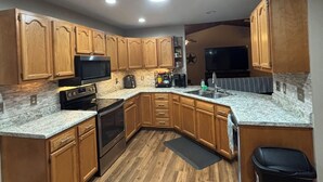 A kitchen with wooden cabinets, a granite countertop, a stainless steel oven, and a microwave. - Rustic Retreat near Norfork Lake (Clarkridge)