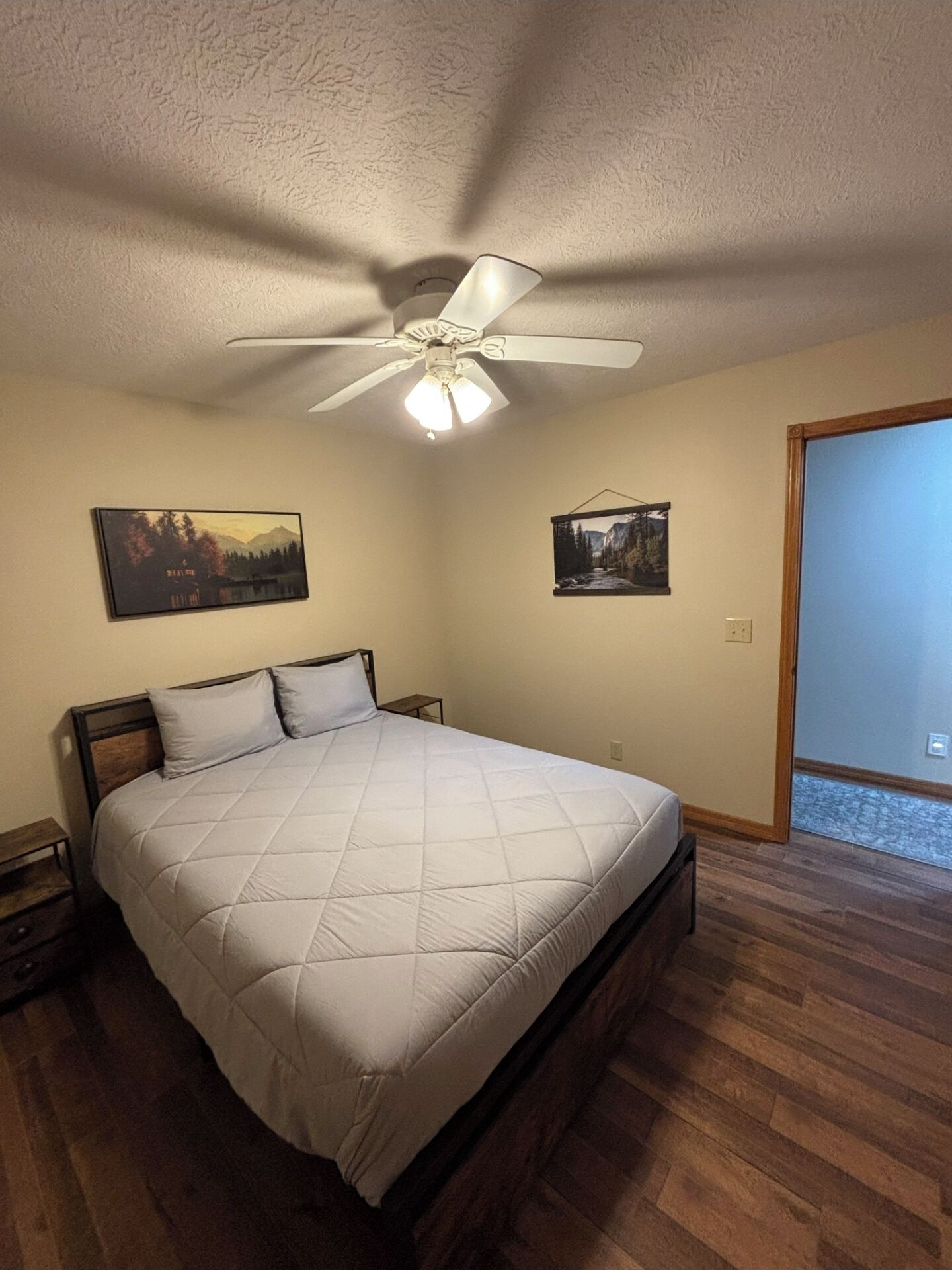 A bedroom with a bed, a ceiling fan, and two framed pictures on the wall.