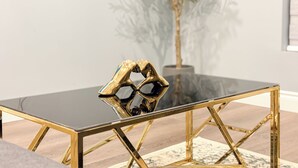 A modern dining table with a glass top and gold frame, set on a wooden floor with a patterned rug.