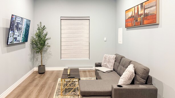 A modern living room with a grey sofa, a coffee table, and a large window with blinds.