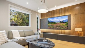 Un salon moderne avec un canapé, une table basse, un téléviseur fixé à un mur en bois et une fenêtre donnant sur des arbres.