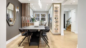 Un espace repas moderne avec une table rectangulaire, des chaises noires, un grand miroir et un mur décoratif en bois.