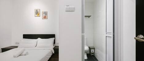 A hotel room with a bed, a nightstand, a small table, and a bathroom visible through an open door.