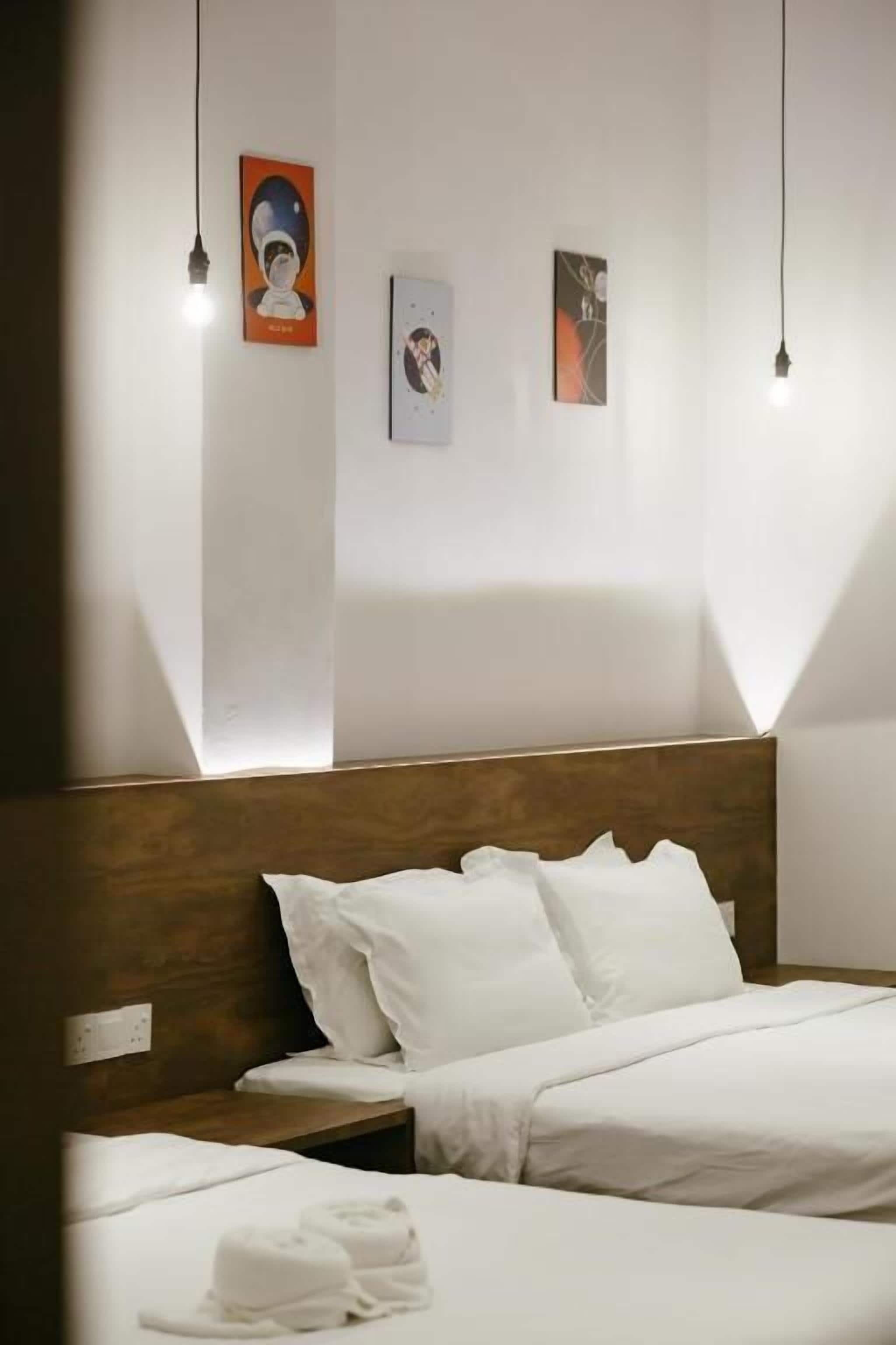 Ein Hotelzimmer mit hölzernem Kopfteil, zwei Betten, weißer Bettwäsche und drei an der Wand befestigten Kunstwerken.