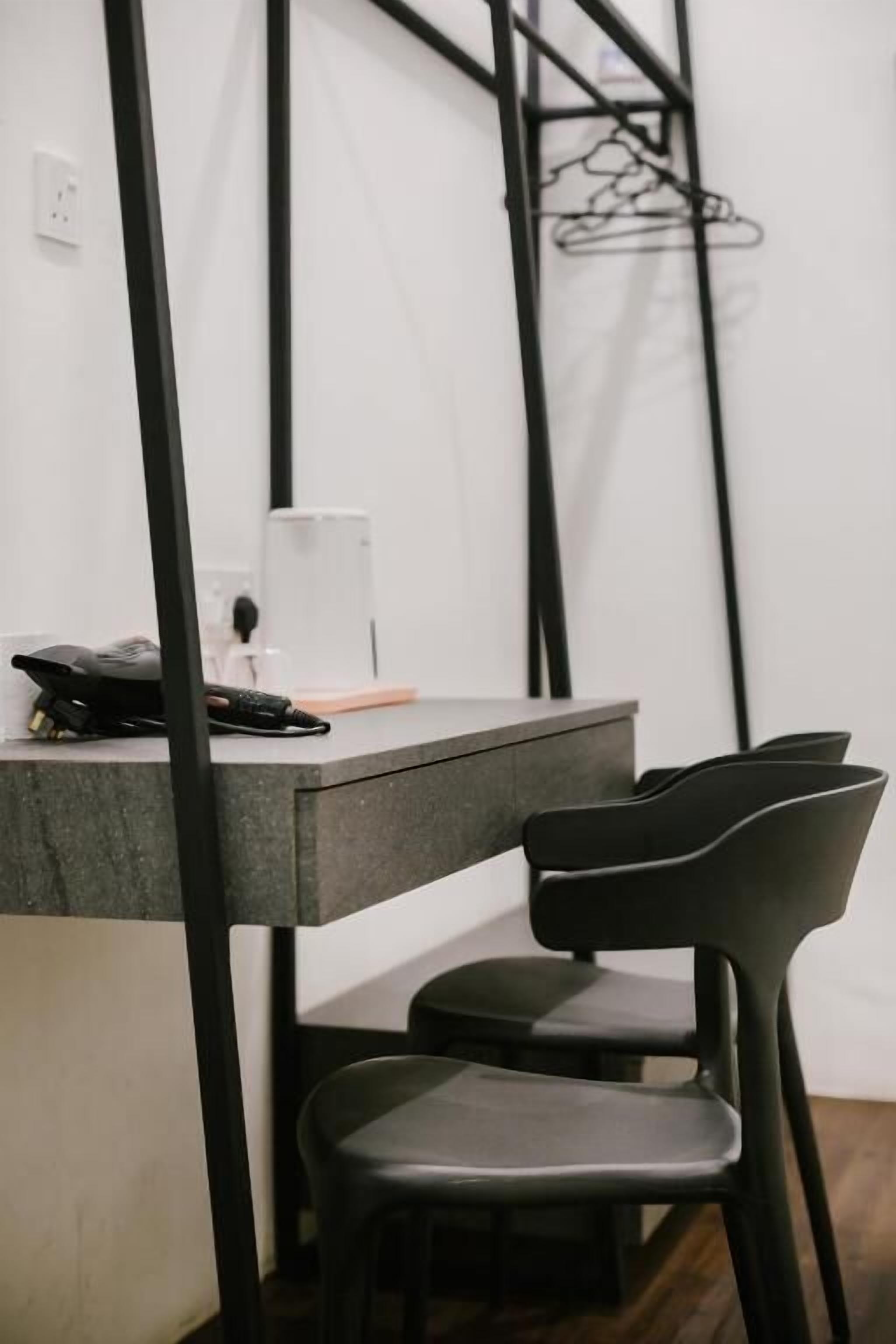 A modern, minimalist room with a grey desk, black chairs, and a simple wall-mounted rack.