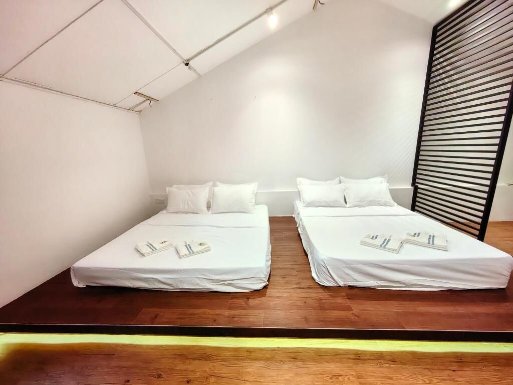 Une chambre avec deux lits simples, un plancher en bois, des murs blancs et un plafond en pente.
