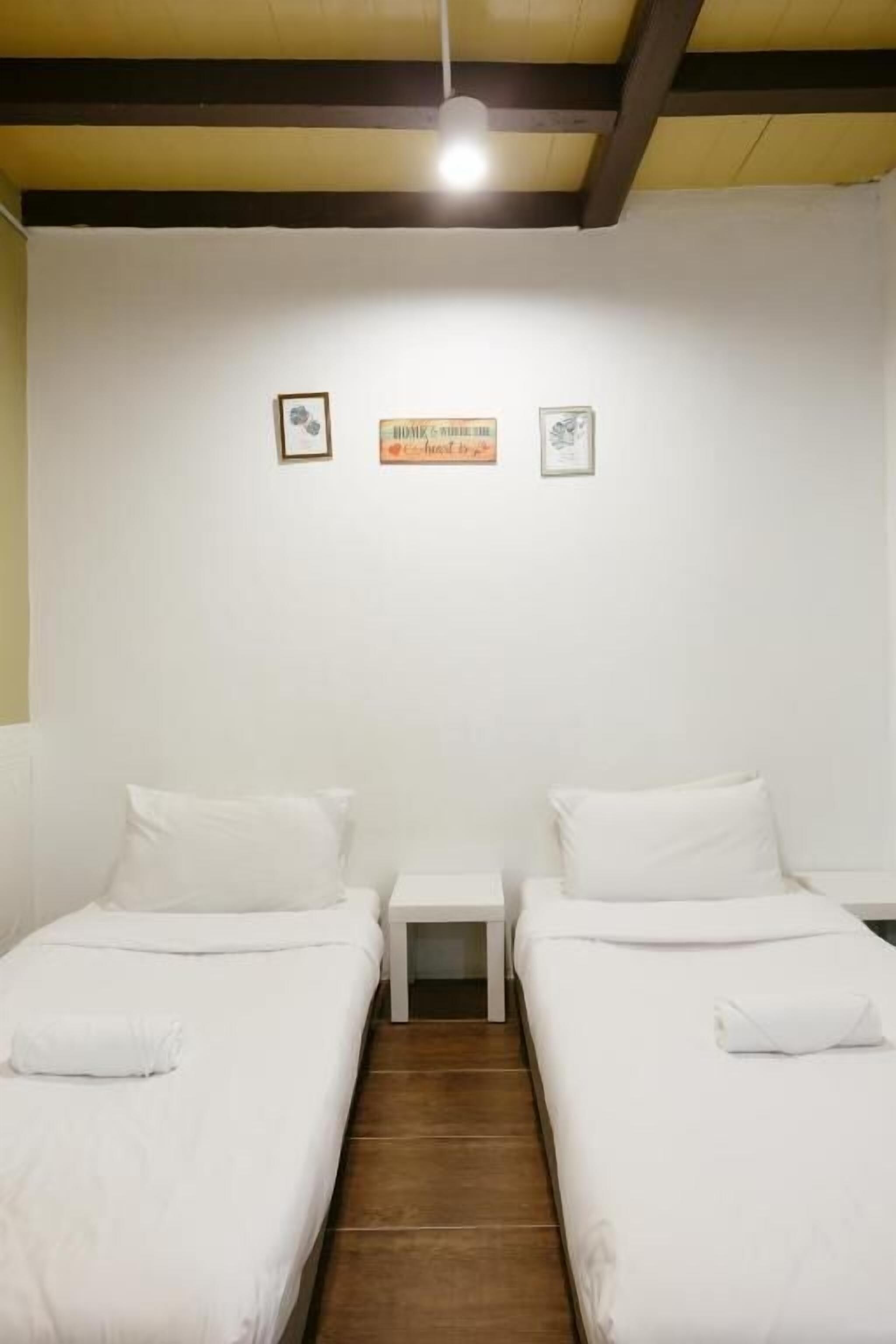 A hotel room with two single beds, a small bedside table, and a wooden ceiling.