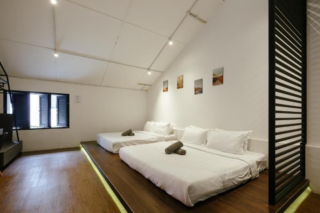 A modern hotel room with two beds, a wooden floor, a window with blinds, and artwork on the wall.