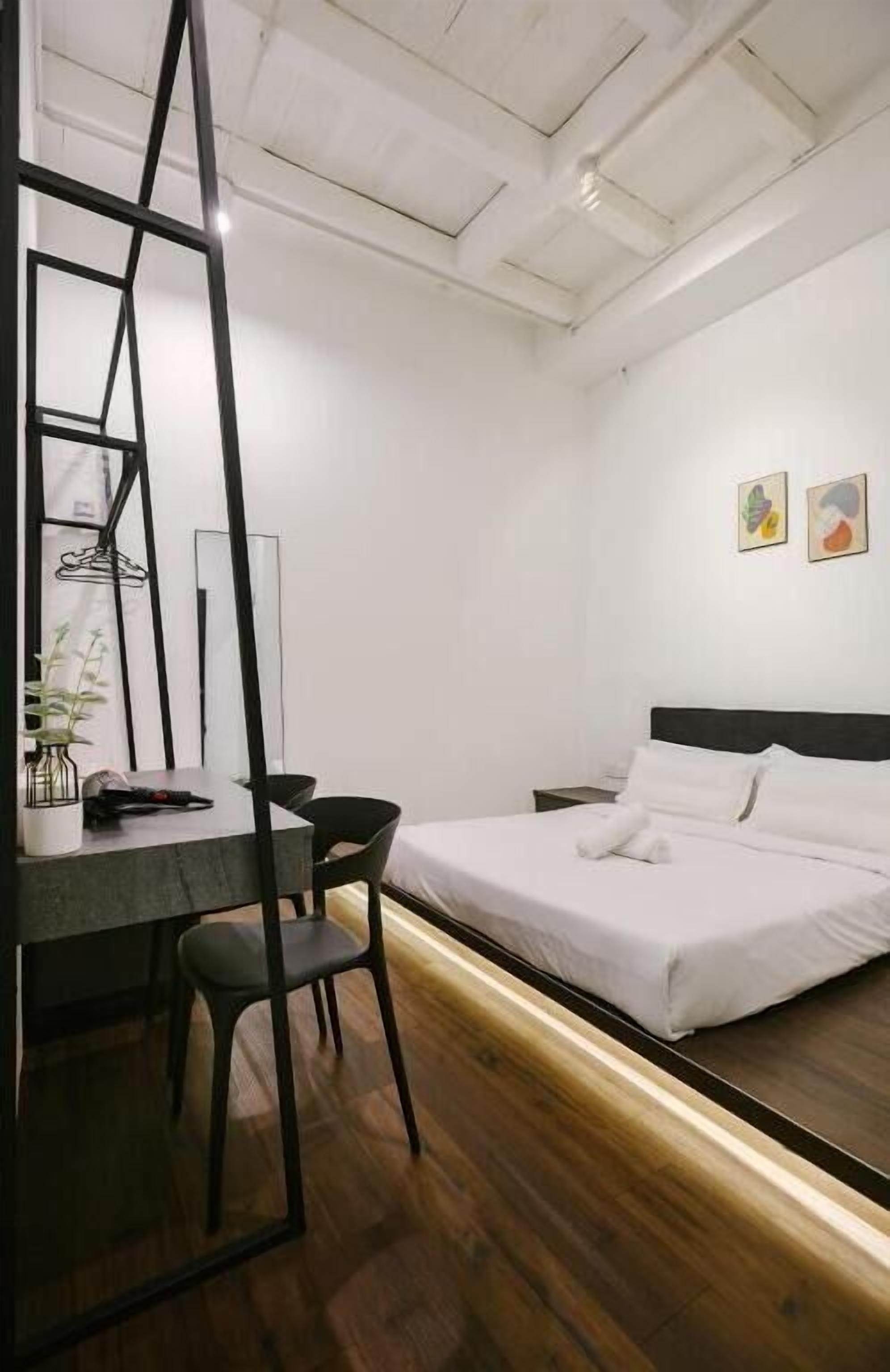 A bedroom with a bed, a desk, a chair, and a mirror.