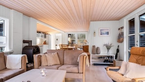 En hyggelig stue med træloft, sofaarrangement, sofabord og pejs.