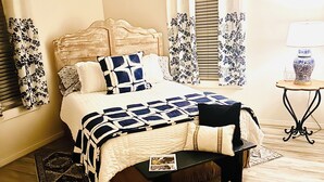 Une chambre à coucher comprenant un lit, une table de chevet, une chaise, une lampe sur pied et un ventilateur de plafond.