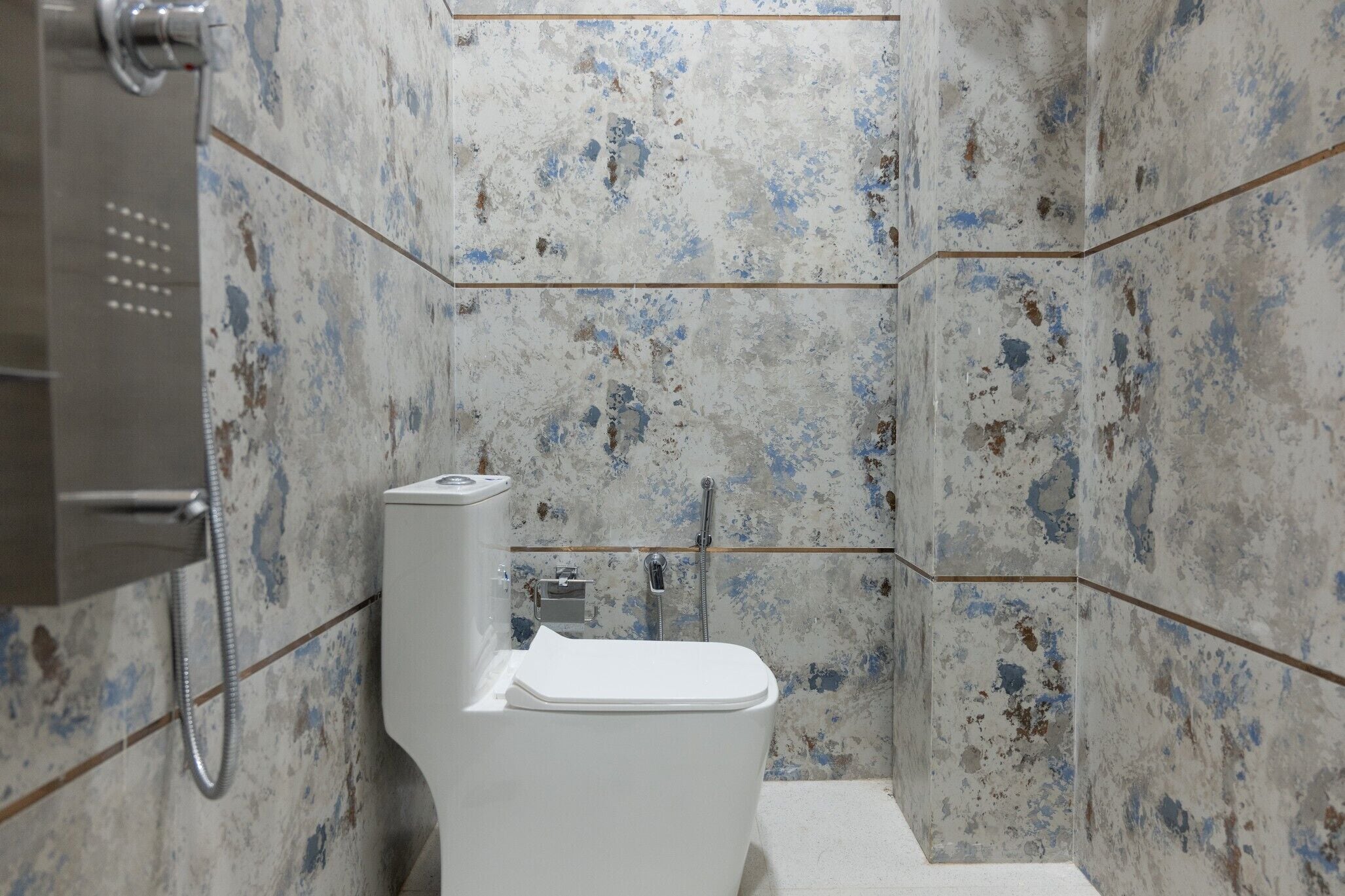 Un baño con inodoro blanco, ducha y pared con superficie texturizada y con manchas.