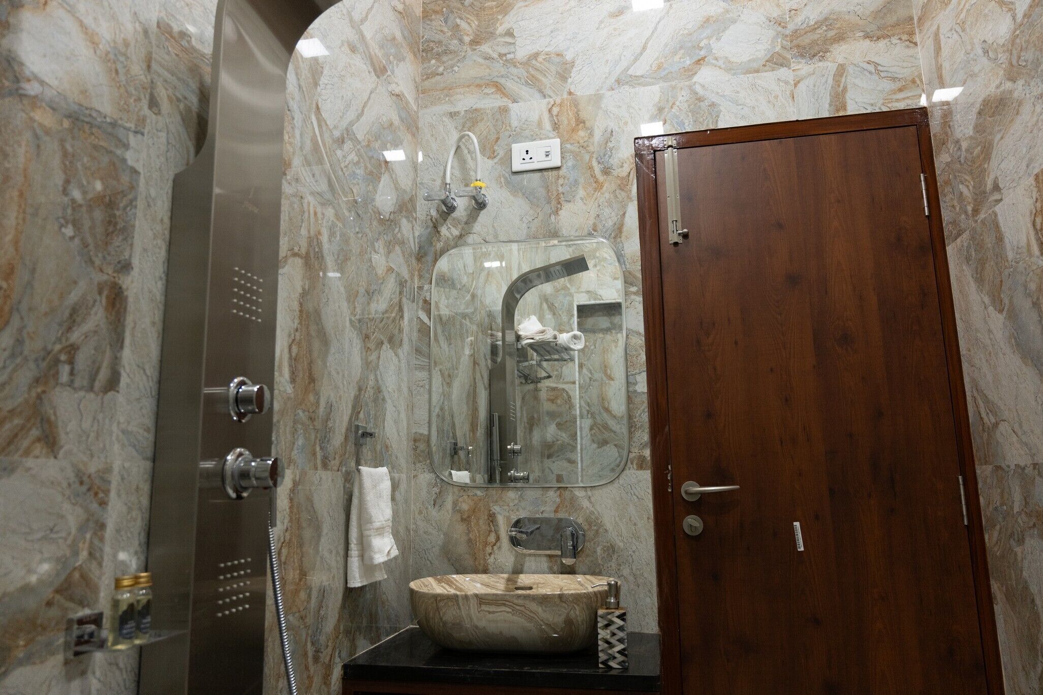 Une salle de bain avec un mur en marbre, une porte en bois, une cabine de douche en verre, un lavabo avec un receveur en marbre et une serviette accrochée au mur.