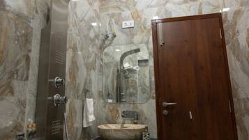Un baño con pared de mármol, puerta de madera, cabina de ducha de vidrio, lavabo de mármol y una toalla colgada en la pared.