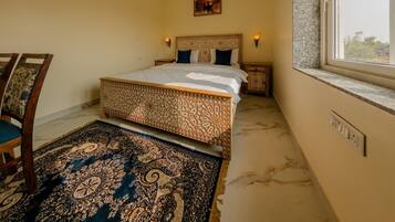 A bedroom with a bed, a nightstand, a chair, a patterned rug, a ceiling fan, an air conditioning unit, a window with a view, and a wall-mounted light fixture.