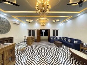 A modern living room with a patterned floor, a blue sofa, a chandelier, and a decorative wall piece. - Vardhan Resorts (Nawalgarh)