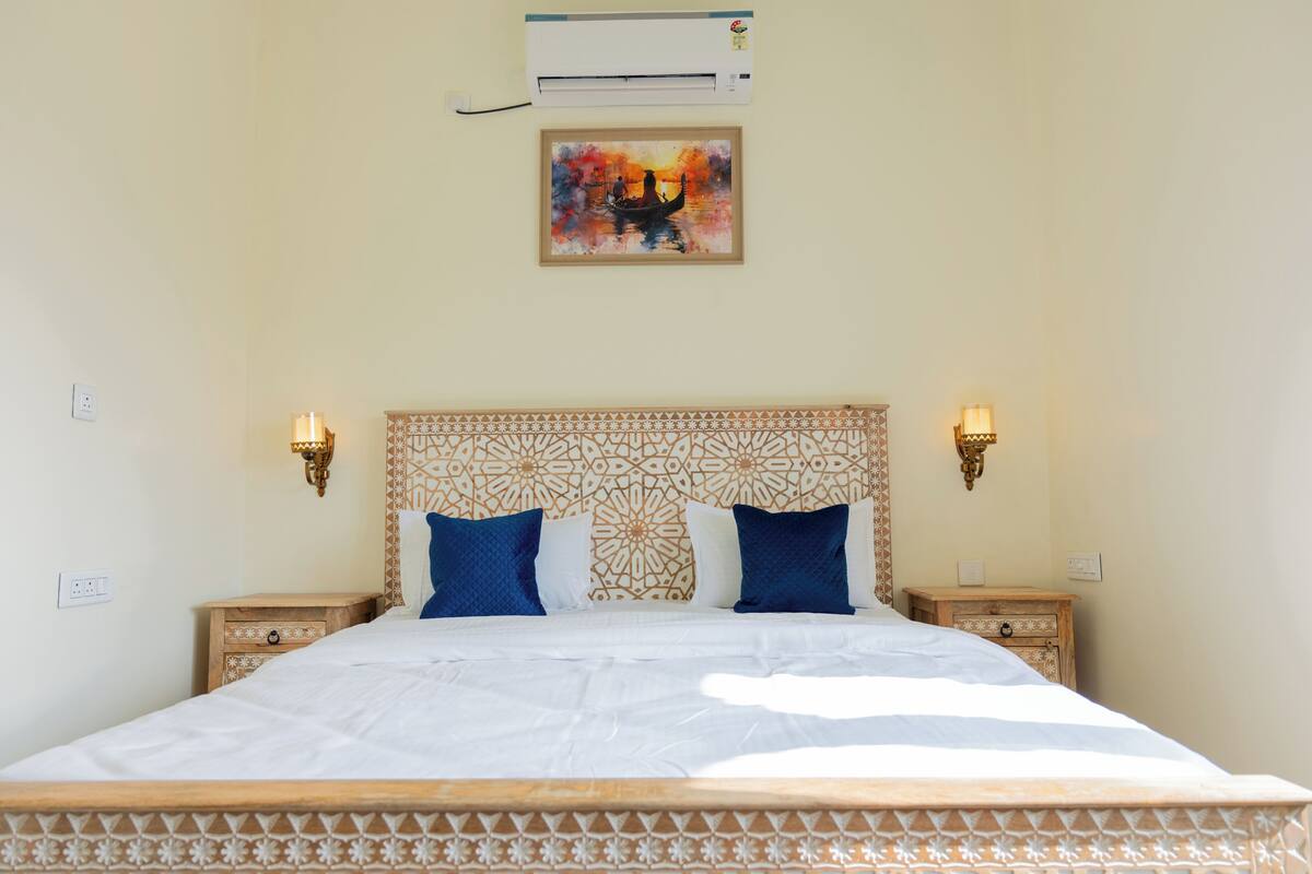 A neatly made bed with a patterned headboard, two bedside tables with wall-mounted lamps, and a framed artwork above the bed.