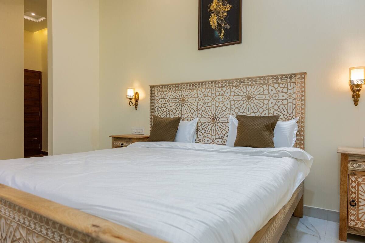 A large bed with a patterned headboard, two bedside tables, and wall-mounted lights.