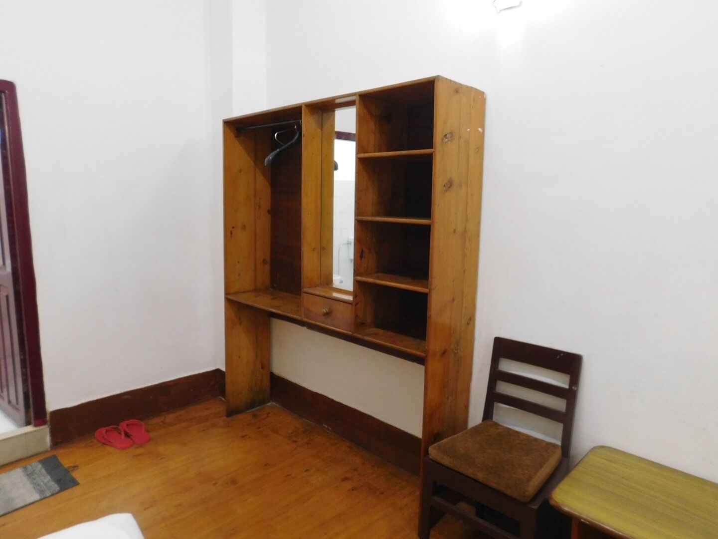 Quarto com guarda-roupa de madeira, cadeira de madeira e uma pequena mesa.