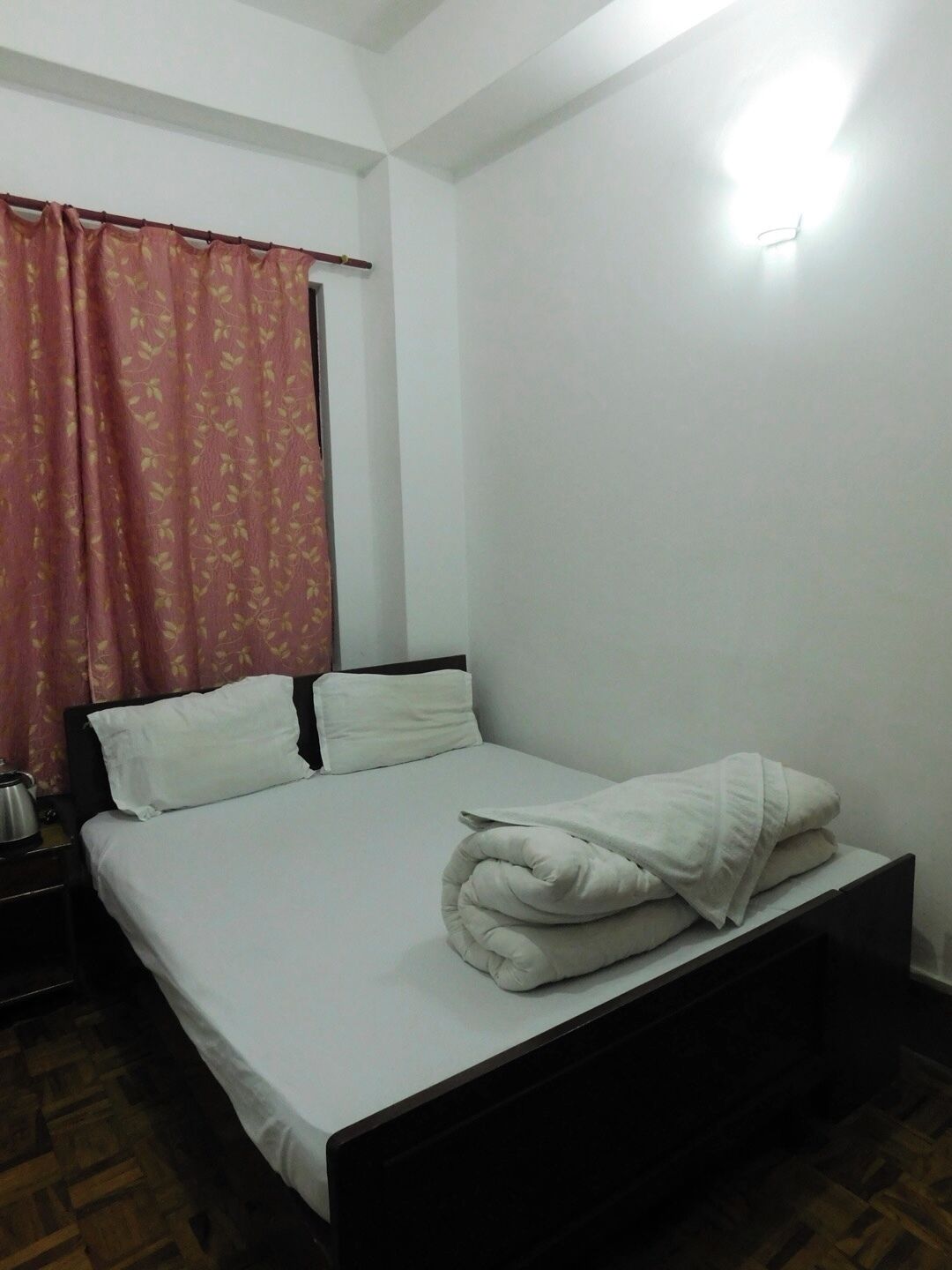 A single bed with white bedding, a wooden headboard, and a nightstand with a kettle.
