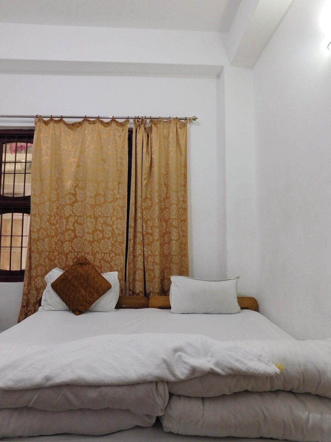 A bedroom with a bed, two pillows, a window with a curtain, and a view of the outside.