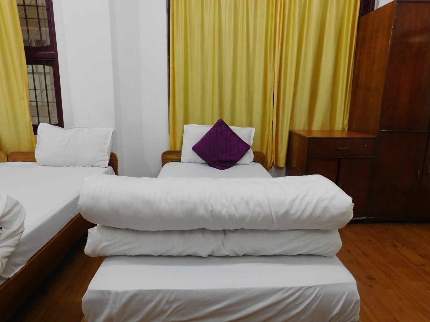 Une chambre d’hôtel avec deux lits simples, une armoire en bois et des rideaux jaunes.