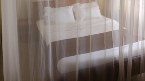 A bed with white bedding, a wooden headboard, and sheer curtains. - Becca Hotel Meru (Meru)