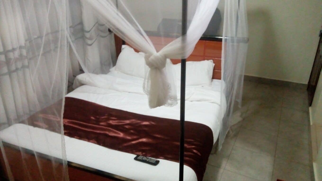 A bed with a canopy, a remote control on the bed, and a brown blanket.